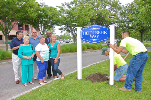 HIghway department workers install a street sign last year along the Peconic River in memory of fallen ambulance volunteer Heidi Behr, as the Behr family — Heidi's grandmother Dorothy, mother June, father John and sister Dana look on. (Credit: Barbaraellen Koch, file)