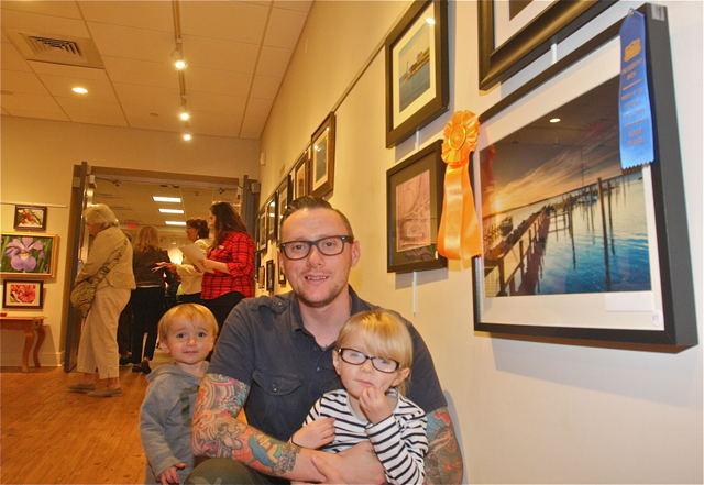 Jon Schusteritsch of Cutchogue posed with his children Max, 1 1/2, and Zoey, 4, by his photo chosen as the Friends Choice award for a landscape scene of docks and the bay at sunrise in New Suffolk. (Credit: Barbaraellen Koch)