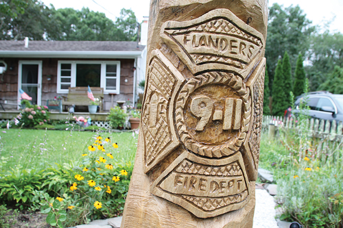PAUL SQUIRE PHOTO | Artist Richard Anderson was commissioned to carve this tribute to Flanders' bravest in a tree in Sue Mastelli's front yard. Mr. Anderson also sculpted the works that line the boardwalk along the Peconic River in downtown Riverhead.