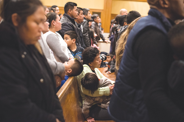 A woman holds a child during Sunday night Spanish language Mass at St. John the Evangelist Church in Riverhead the weekend after the election. It was a trying time for our local immigrant Hispanic community and I believe this image of the packed church captured both uncertainty and faith. (Credit: Kevin Urgiles)
